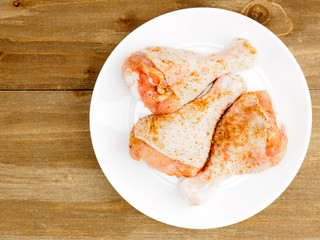 Raw chicken drumsticks in masala powder on white ceramic plate with copy space. Healthy eating concept