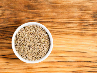Cumin (jeera) seeds in white bowl on brown wood background with copy space. Healthy eating, ayurveda, naturopathy concept