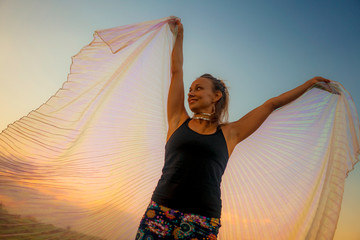 Fototapeta na wymiar young attractive and happy woman in yoga clothes spreading wings cloth under a beautiful sunset sky carefree and joyful in wellness and freedom concept