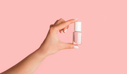 Unrecognizable young girl holding bottle of nail polish on pink background, closeup. Panorama