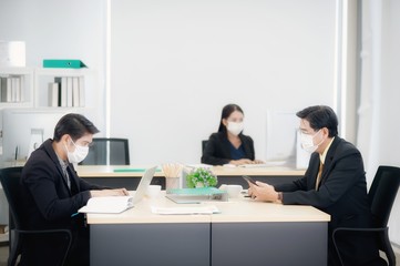 Asian business people working in the office during the coronavirus or covid 19 spread in China and spread around the world. Employees must wear a medical mask and keep a distance to prevent infection.