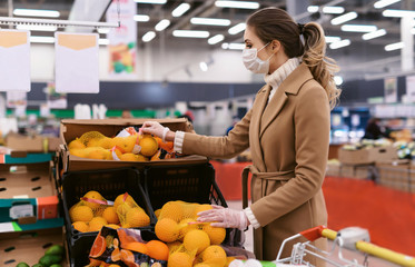 Shopping during the coronavirus Covid-19 pandemic. A young woman buys food in a supermarket. Woman in facial mask and gloves to prevent infection.