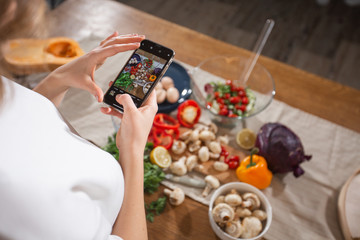 Woman take a picture of different beautiful vegetables and greens with a mobile phone at her kitchen. Smartphone food photography. Healthy eating, vegetarian food, dieting . for weight loss and detox.