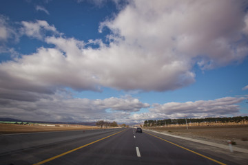 Asphalt road and bright blue sky with fluffy clouds . Empty desert asphalt road from low angle with mountains and clouds on background. road, red desert landscape . Open road with blue clouds .