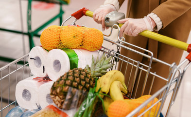 Coronavirus 2020 pandemic. Close up of woman hands in medical disposable gloves with a supermarket cart. People goes to the market to buy food during quarantine. Covid 19 epidemic over the World