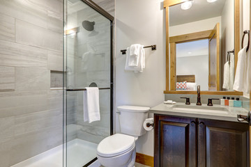 Natural new classic bathroom interior with new glass and ceramic tiles walk in shower and grey walls with white towels.