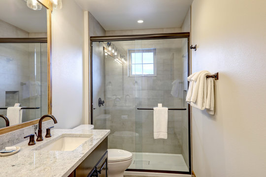 Natural new classic bathroom interior with new glass and ceramic tiles walk in shower and grey walls with white towels.