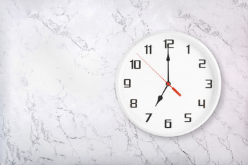 White round wall clock on white natural marble background. Seven o'clock, 7 a.m. or 7 p.m.