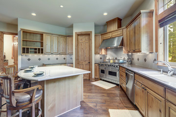 Bright wooden large kitchen interior with island with three chairs and white grey backsplash.