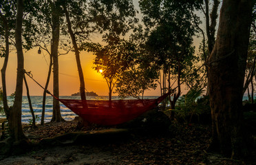A hammock on the beach with trees all around at sunrise on the White Beach, Koh Rong, Cambodia