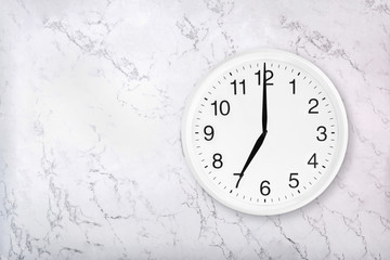 White round wall clock on white natural marble background. Seven o'clock. 7 a.m. or 7 p.m
