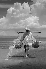 Kusamba, Bali, Indonesia - March 11, 2010 : A local balinese woman spraying water on the beach for...