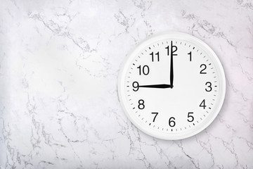 White round wall clock on white natural marble background. Nine o'clock. 9 a.m. or 9 p.m