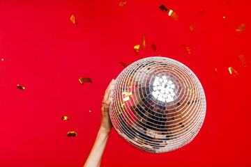 Female hand holds a disco ball on a bright red background and gold glitters fly