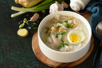 Arroz Caldo Soup. Hot soup with ginger chicken rice and garlic in a bowl on a dark countertop. Copy space.