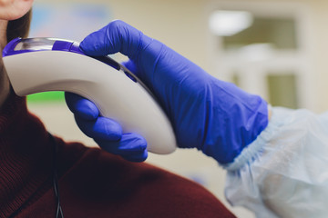 The doctor hand in a protective glove holds an infrared thermometer and measures the temperature of...