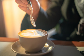 hand with a spoon over a cup of coffee blurred image