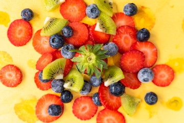 ripe, fresh, natural red cut strawberries blueberries and kiwi bunch, a healthy spring and summer fruit, on yellow background