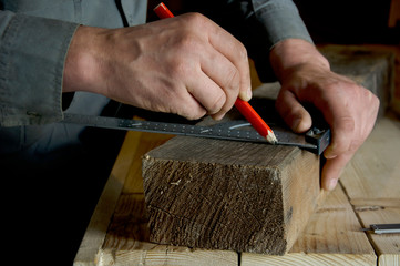 carpenter with a pencil and a ruler marks the cut line on the wooden beam