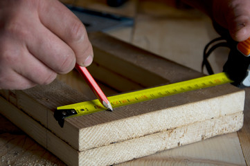 carpenter measures a wooden board with a tape measure and notes with a pencil