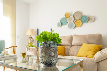 Beautiful living room. Selective focus on the artificial plant in the foreground.  Blurry background. Beige, turquoise, brown and yellow color palette.