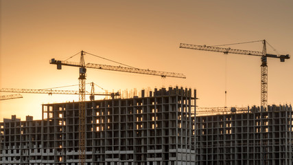 Construction site with cranes at orane yellow sunset. Working with installation metal