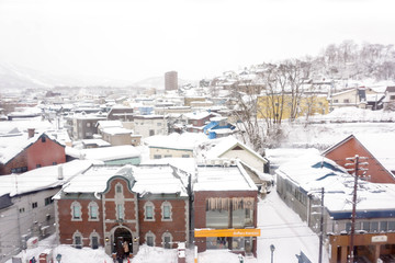 Otaru, Hokkaido prefecture, Japan, February 14 2018 : Closeup and crop high angle view of snow capped Otaru city and Sakaimachi shopping street with tourists on winter foggy sky background.