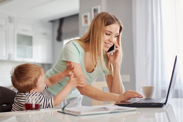 Young mother feeding child and talking on the phone