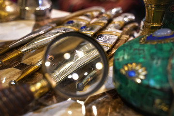 Examining details on traditional daggers through loupe magnifying glass in vintage antiques shop, close up detail