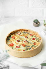 Homemade cheesy spinach quiche for brunch. set on white cafe table background.