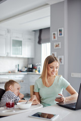 Mother feeding toddler and using gadgets