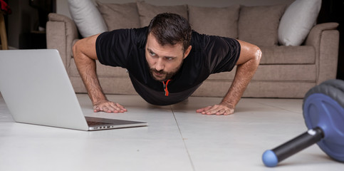 Young man exercising and working out online with laptop or phone at home during covid-19 pandemic quarantine. Sports and healthy lifestyle concept