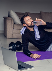 Young man exercising and working out online with laptop or phone at home during covid-19 pandemic...