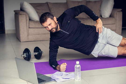 Young Man Exercising And Plank Working Out Online With Laptop Or Phone At Home During Covid-19 Pandemic Quarantine. Sports And Healthy Lifestyle Concept