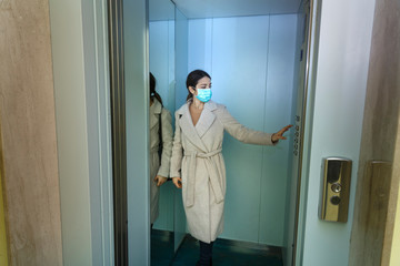 Ragazza con cappotto e mascherina di protezione prende l'ascensore con aria seria