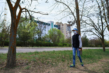 Fototapeta premium child girl walks down the street during the day, a pedestrian walkway and high-rise buildings with apartments, a residential area, a medical mask on her face protects against viruses and dust