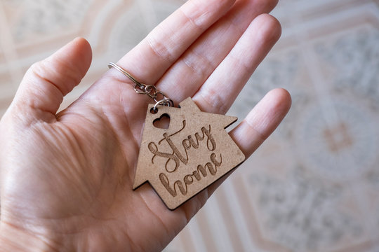 Closeup of a hand holding a wooden keychain with the engraved message stay home - Powered by Adobe