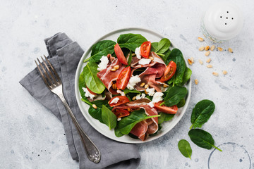 Spring Salad with spinach, cherry tomato, mozzarella, pine nuts and ham with olive oil in a simple ceramic plate on an old concrete gray background.