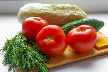 Tomatoes cucumbers cabbage and dill lie on a cutting Board on a white background.