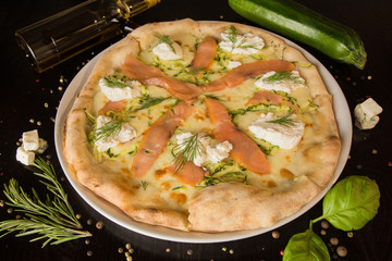 Ricotta pizza - with salmon, various types of cheese and herbs. On a black table with sprinkled spices and ingredients. Photo for the menu.