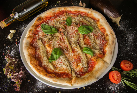 Pizza with eggplant and basil, tomato paste, grated cheese, without meat. On a black table with scattered spices and ingredients. Photo for the menu.