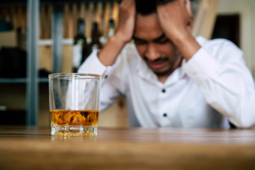 Depressed stressed and lonely man sitting in the dark facing with unemployment financial crisis and family divorce or personal problem and sadness with a glass of whiskey, alcoholic, alcohol addiction
