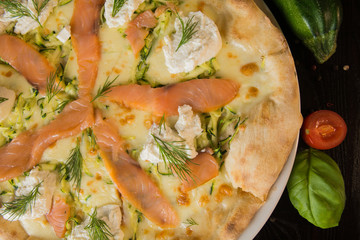 Salmon pizza - top view, on a black table, shot in three quarters, next to the ingredients