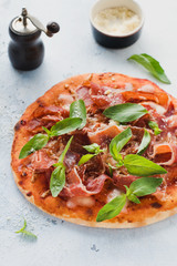 Homemade pizza with jamon, mozzarella and fresh basil leaves on a light concrete old background. Top view.