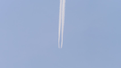 Large passenger supersonic plane flying high in air polluted blue sky, leaving long white trail.