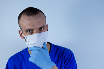 doctor in a protective mask on a blue background. Thinking over the treatment, holding a gloved hand near the mouth.copyspace for text.