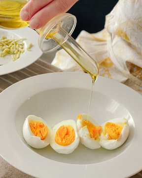 Boiled eggs on white plate with woman pouring extra virgin olive oil