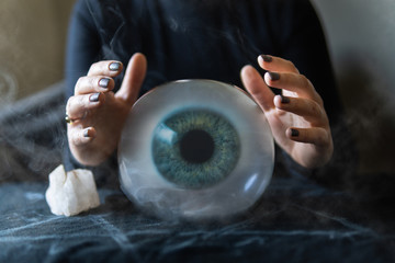 Fortune teller holds hands above magic crystal ball with eyeball inside. Conceptual image of black magic and occultism