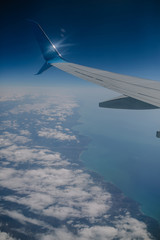 Fototapeta premium wing of the plane against the background of the sea and clouds. view from the airplane eluminator. sunny weather overboard. blue sky blue sea