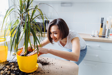 Beautiful smiling girl with braces replanting a indoor flower. Wearing a white T-shirt and blue...